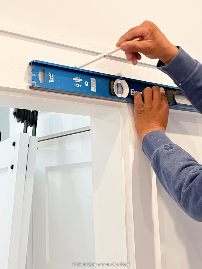 measuring for barn door track with a level and pencil on door header