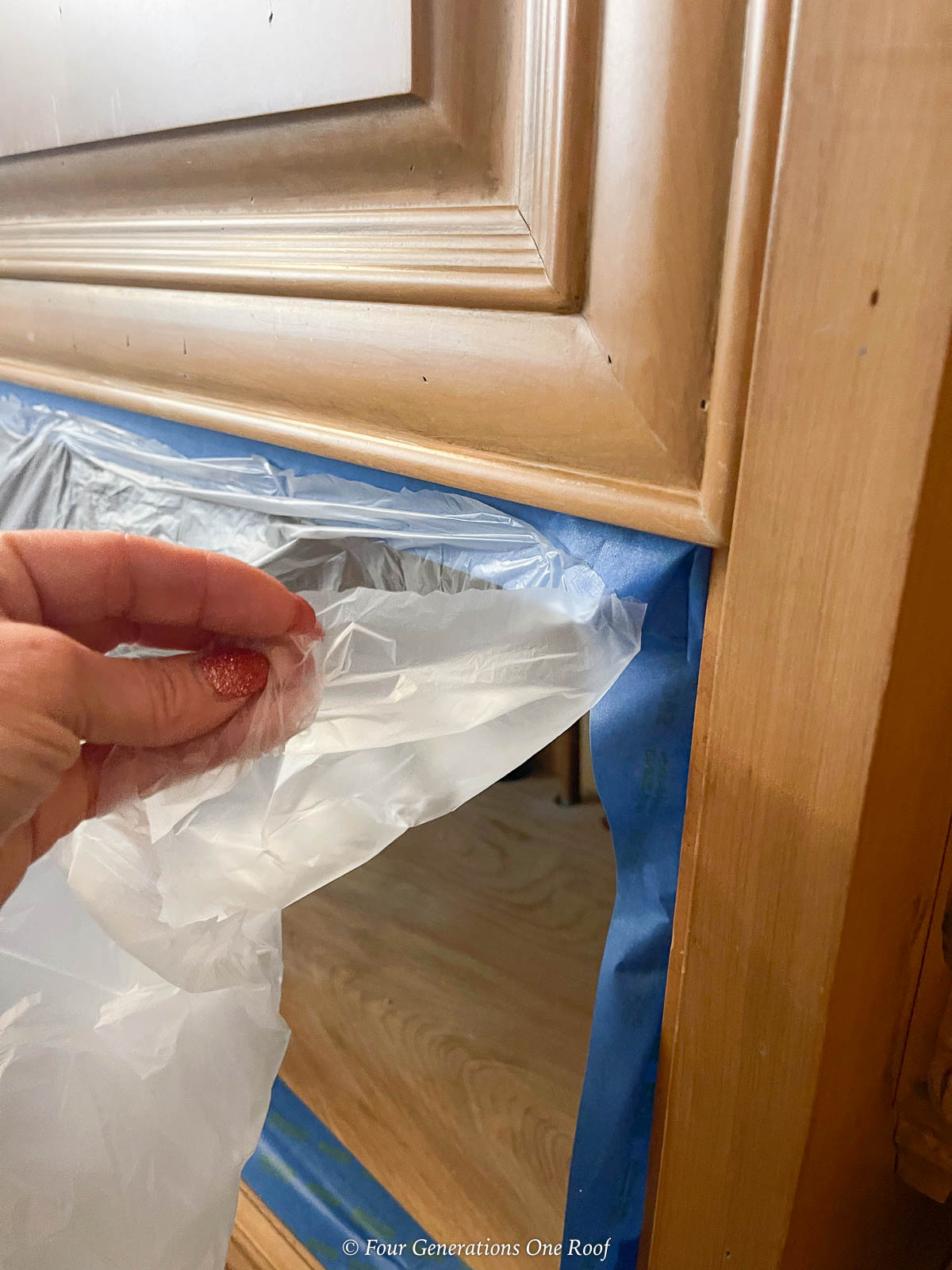 taping-kitchen-cabinet-drawers-with-plastic-to-prepare-spray-painting-kitchen-cabinets