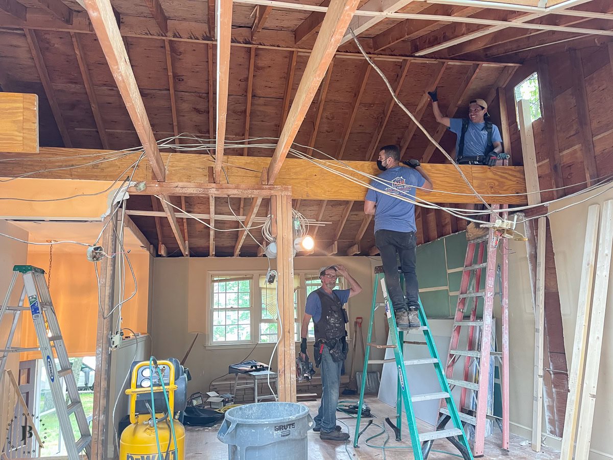 Contractors installing a load-bearing beam between a kitchen and living room to create an open-concept space