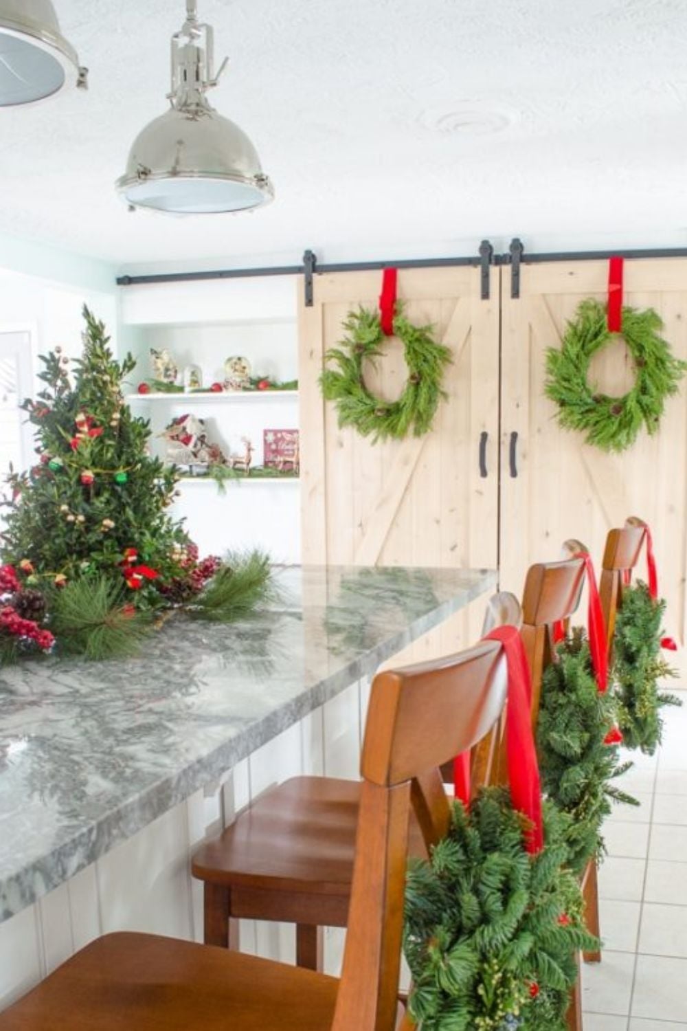 Budget-friendly Christmas kitchen with fresh greenery garland on white cabinets and wreaths on counter stools