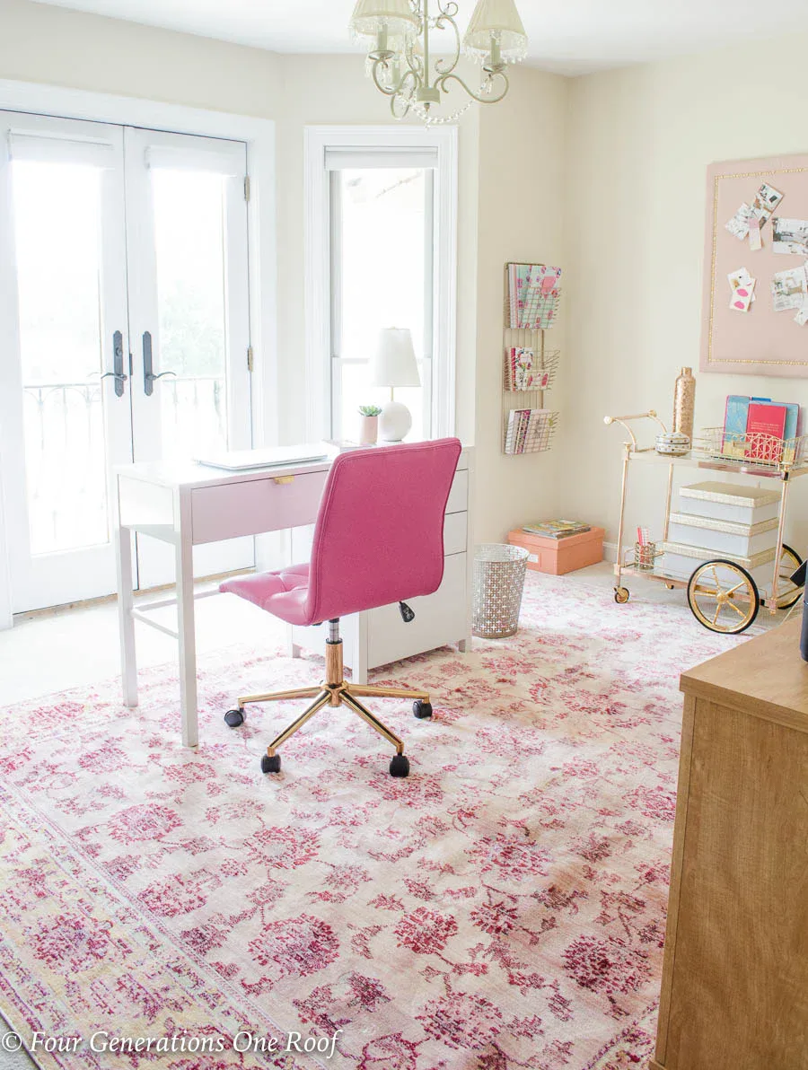 Feminine workspace with gold bar cart storage, pink rug, and white desk in girly office design