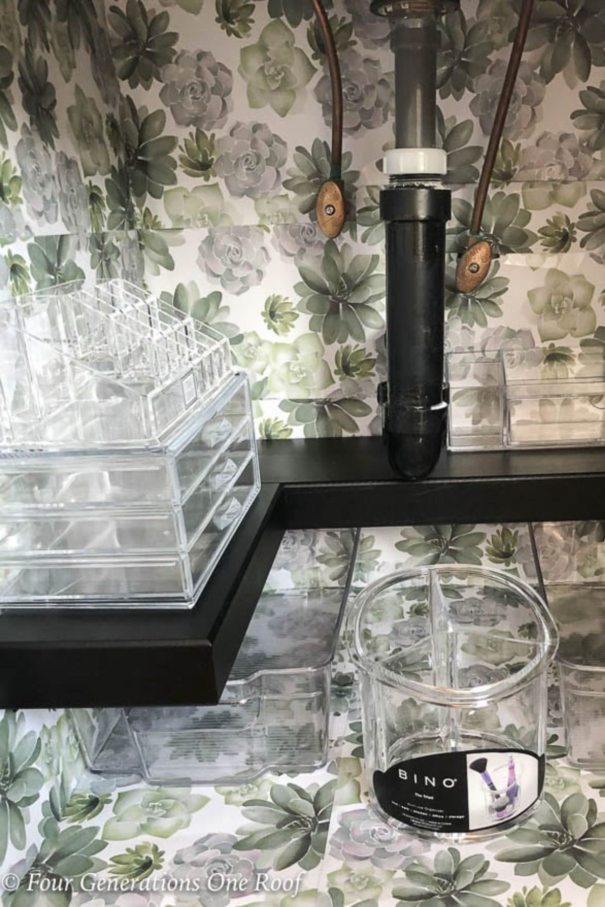under bathroom sink lined with green flower drawer liner, black premade shelf and acrylic organizers 